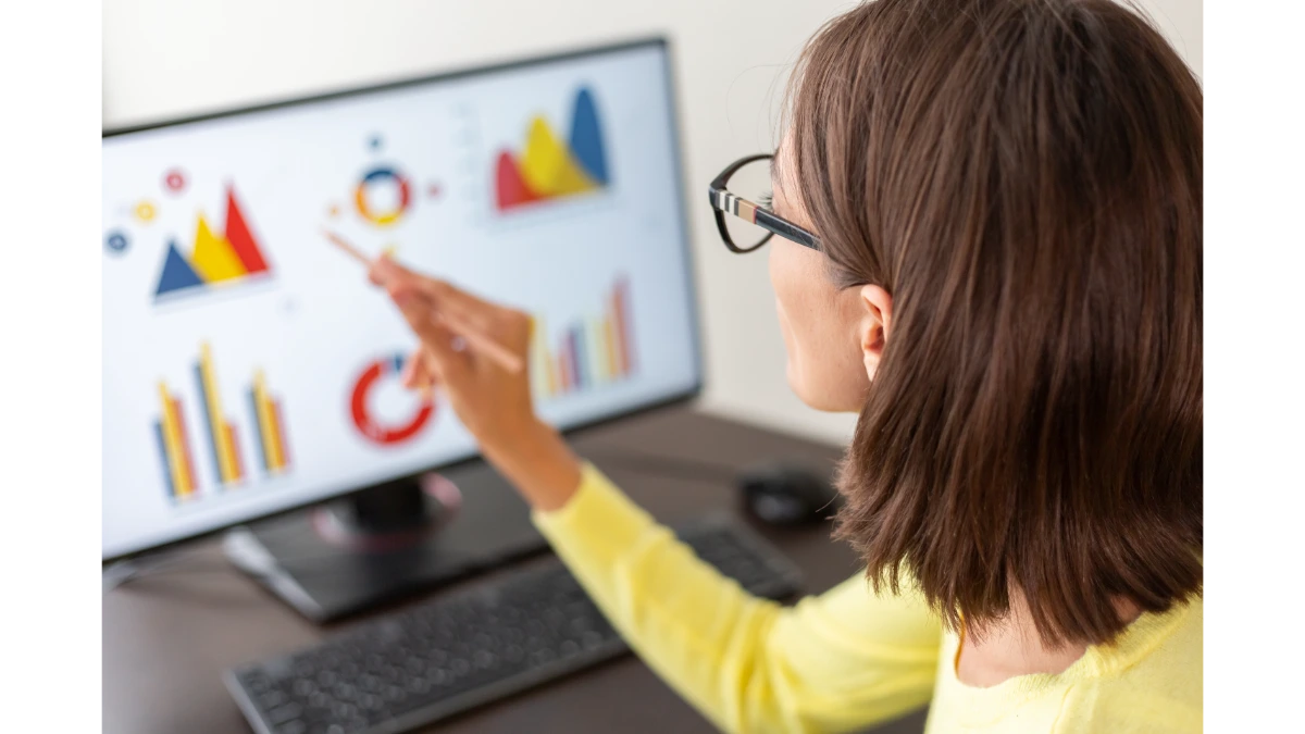 Persona analizando gráficos y métricas en un monitor, señalando un panel de datos con diagramas y estadísticas.
