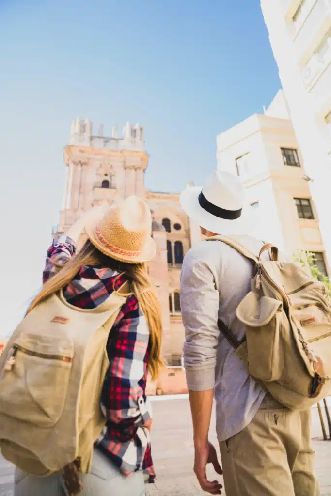 Turismo accesible: cómo diseñar experiencias culturales inclusivas para todas las personas 5 Dos viajeros con mochilas y sombreros contemplan la arquitectura de una catedral histórica durante una visita turística.