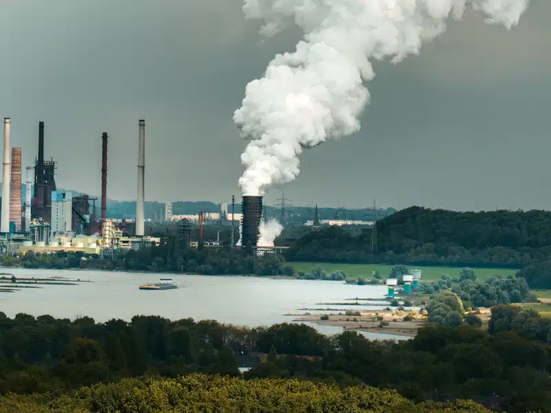 Salud ambiental: cómo la química ayuda a prevenir los riesgos de la contaminación 3 Complejo industrial junto a un río con chimeneas de emisiones visibles