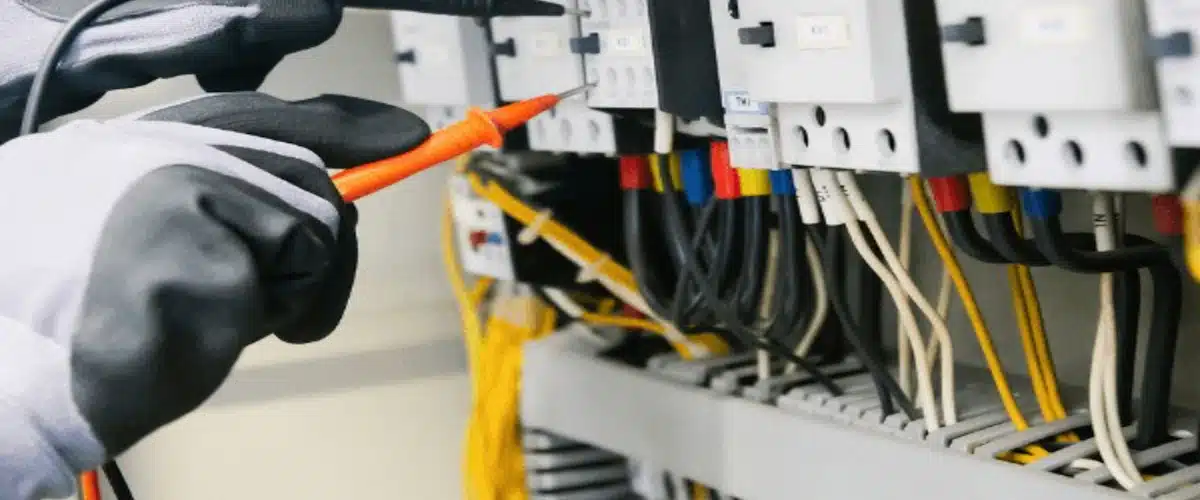 Electricista con guantes comprueba el cableado de un cuadro eléctrico