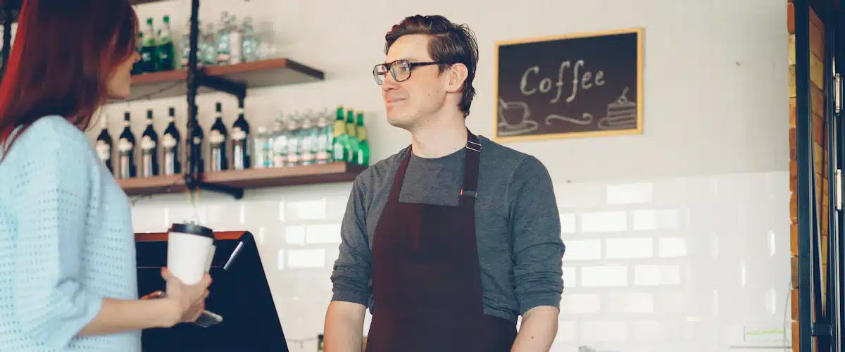 Atención al cliente: 7 estrategias para mejorar la experiencia 6 Empleado de cafetería atendiendo a una clienta que paga con el móvil