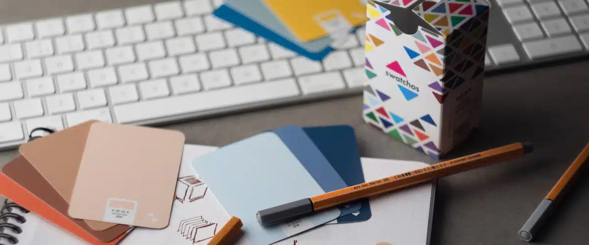 Identidad visual corporativa: elementos para construir una marca coherente 7 Muestras de colores impresas junto a teclado y lápices sobre escritorio