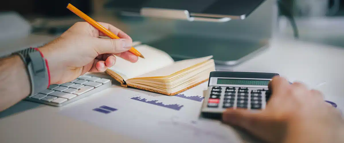 Persona trabaja con una calculadora y un cuaderno sobre su escritorio