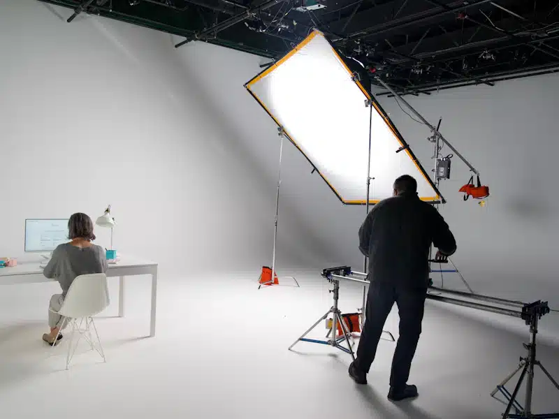Producción audiovisual: fases, equipos y planificación de un proyecto 3 Profesionales graban una escena con cámara y luces en un plató blanco