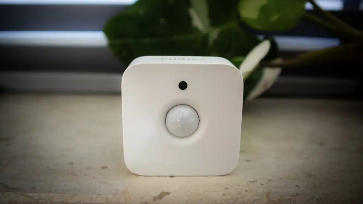 Sensor blanco de movimiento apoyado junto a plantas y una ventana iluminada