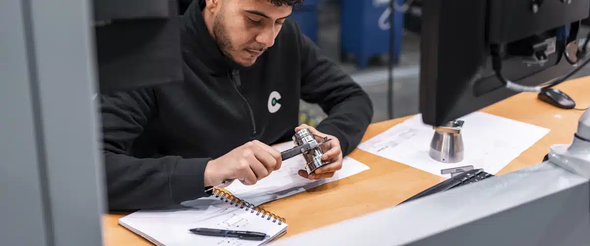 Oficina técnica: qué es, funciones y cómo gestionar proyectos 7 Técnico mide una pieza metálica con calibre frente a dibujos industriales