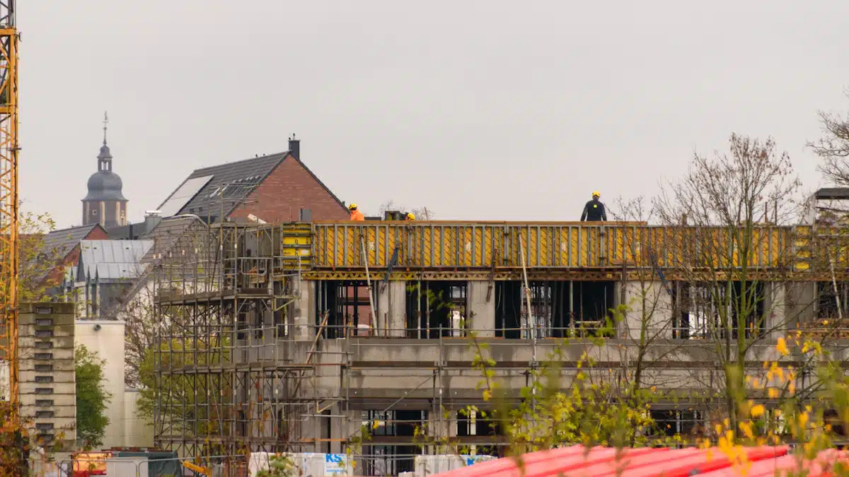 Jefe de obra: funciones, requisitos y control de acabados 4 Trabajadores y grúa junto a la estructura de un edificio en construcción